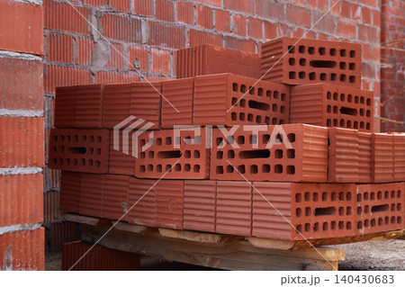 Stack of red perforated construction bricks placed on wooden pallets at an active building site 140430683