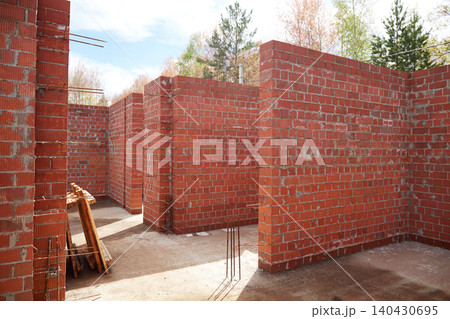 Wide interior view of an unfinished brick house with multiple rooms and exposed reinforcement bars Wide interior view of an unfinished brick house with multiple rooms and exposed reinforcement bars 140430695