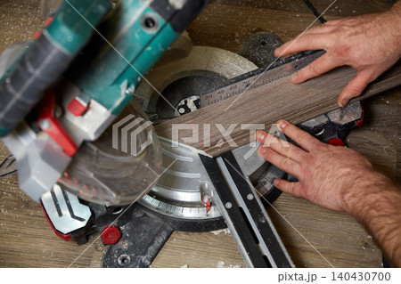 Construction worker cuts wood plank using power saw in workshop Construction worker cuts wood plank using power saw in workshop 140430700