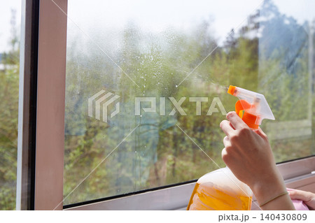A person sprays cleaning liquid onto a dirty window using a spray bottle while preparing to wipe the glass surface A person sprays cleaning liquid onto a dirty window using a spray bottle while preparing to wipe the glass surface 140430809