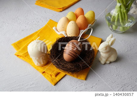 Multicolored Easter eggs in a nest and on a tray next to white candles 140430857