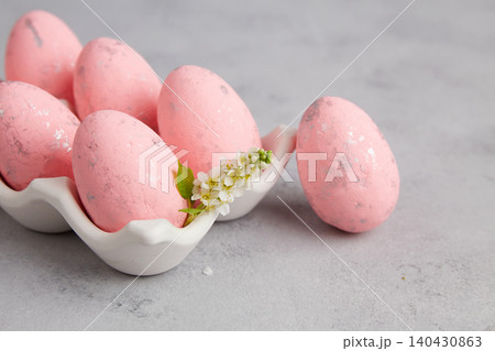 Bright pink eggs sit in a white tray. Small white flowers and green leaves are next to the eggs. Bright pink eggs sit in a white tray. Small white flowers and green leaves are next to the eggs. 140430863