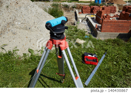 Surveying level on tripod at construction site near brick foundation. 140430867