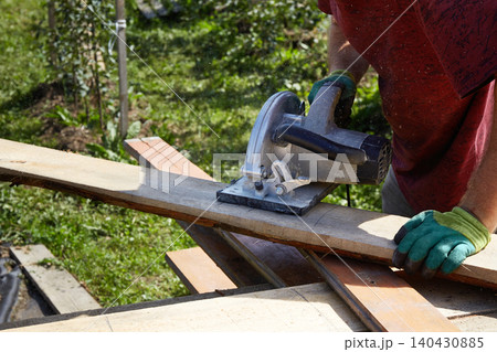 Worker cutting a wooden plank with a circular saw outdoors Worker cutting a wooden plank with a circular saw outdoors 140430885