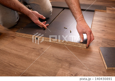 Man assembling furniture on wooden floor, connecting panels with screws. Man assembling furniture on wooden floor, connecting panels with screws. 140430891