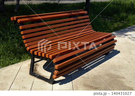 A wooden bench made of slats rests on a stone pathway in a park. A wooden bench made of slats rests on a stone pathway in a park. 140431027