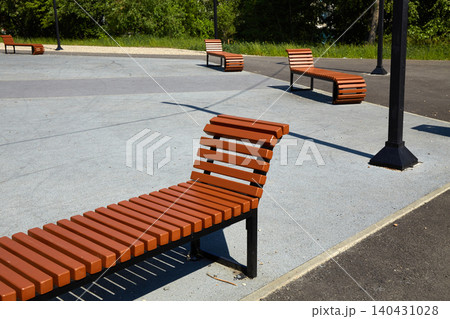 Several wooden benches placed on a concrete surface in a public park during daytime Several wooden benches placed on a concrete surface in a public park during daytime 140431028