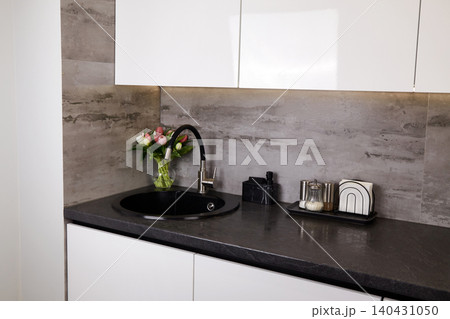 A kitchen space shows a black sink with a faucet and a vase of flowers on the counter. A kitchen space shows a black sink with a faucet and a vase of flowers on the counter. 140431050