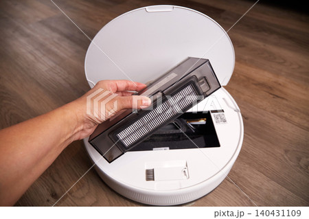 A hand removes the dustbin from a robot vacuum cleaner in a home setting. A hand removes the dustbin from a robot vacuum cleaner in a home setting. 140431109