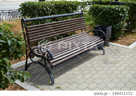 A wooden bench made of slats rests on a stone pathway in a park. A wooden bench made of slats rests on a stone pathway in a park. 140431152