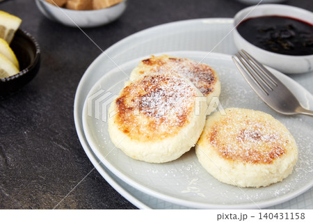 Three cottage cheese pancakes with jam lie on a gray plate Three cottage cheese pancakes with jam lie on a gray plate 140431158