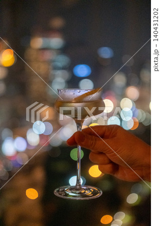 A hand holding a glass of cocktail with colorful night city view on the background A hand holding a glass of cocktail with colorful night city view on the background 140431202