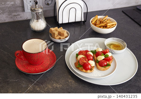 Bruschetta Caprese with mozzarella, cherry tomatoes, and basil on a plate. A cup of coffee and sugar nearby. Bruschetta Caprese with mozzarella, cherry tomatoes, and basil on a plate. A cup of coffee and sugar nearby. 140431235