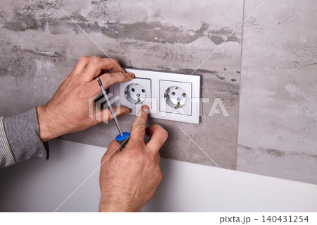 A man uses a screwdriver to install an electrical outlet on a porcelain tile wall A man uses a screwdriver to install an electrical outlet on a porcelain tile wall 140431254