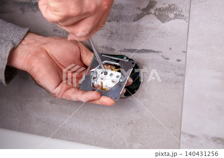 Electrician installing electrical outlets in a wall made of porcelain tiles. Electrician installing electrical outlets in a wall made of porcelain tiles. 140431256