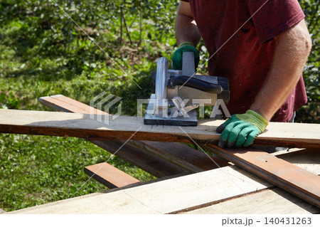 Skilled worker using a circular saw to cut wooden planks in a sunny outdoor setting Skilled worker using a circular saw to cut wooden planks in a sunny outdoor setting 140431263