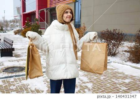 Happy young woman stands near shopping mall with shopping bags in winter 140431347