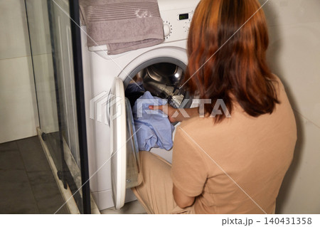 Woman loading clothes into a front-loading washing machine at home 140431358