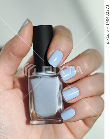 Hand holding pale cornflower blue nail polish bottle. Female fingers with pastel creme manicure holding lacquer bottle close up. Spring and winter fashion cosmetic swatch preview for beauty salon Hand holding pale cornflower blue nail polish bottle. Female fingers with pastel creme manicure holding lacquer bottle close up. Spring and winter fashion cosmetic swatch preview for beauty salon 140432273