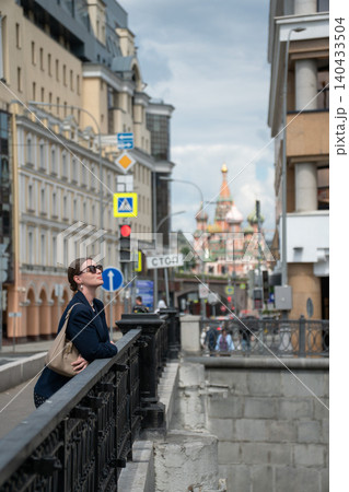 Woman leans on bridge railing in Moscow with Saint Basils Cathedral, urban lifestyle, cultural heritage, travel atmosphere in iconic city setting. Tourism, destination, city lifestyle content, travel Woman leans on bridge railing in Moscow with Saint Basils Cathedral, urban lifestyle, cultural heritage, travel atmosphere in iconic city setting. Tourism, destination, city lifestyle content, travel 140433504