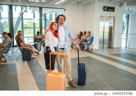Couple smiling and waiting with luggage at airport terminal 140433596