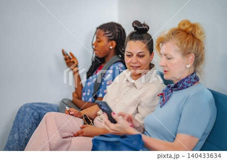 Diverse women sitting in waiting room using smartphones Diverse women sitting in waiting room using smartphones 140433634