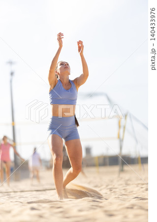 Young woman practices beach volleyball while others play in sunny day at sandy court near ocean 140433976