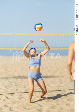 Woman plays beach volleyball while enjoying sunny weather at the sports court near the ocean Woman plays beach volleyball while enjoying sunny weather at the sports court near the ocean 140434023
