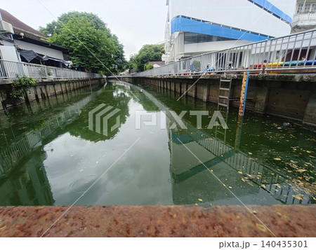 Urban canal waterway, concrete bank, calm reflection, green water, drainage channel, city landscape 140435301