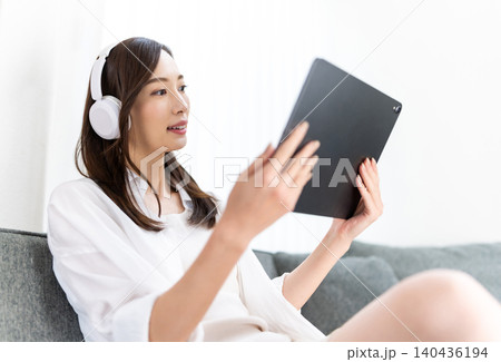 ソファでタブレットとヘッドホンを楽しむ女性 ソファでタブレットとヘッドホンを楽しむ女性 140436194