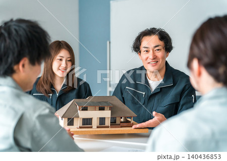 住宅模型を使って商談,説明,プレゼンする作業服姿の建設業,建築業の男女のビジネスマン 住宅模型を使って商談,説明,プレゼンする作業服姿の建設業,建築業の男女のビジネスマン 140436853