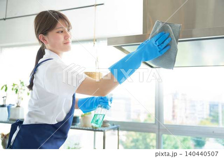 キッチン周りの油汚れを専用洗剤で丁寧に除去する若い女性 キッチン周りの油汚れを専用洗剤で丁寧に除去する若い女性 140440507
