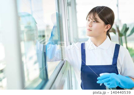 窓を丁寧に拭くエプロン姿の若い女性 窓を丁寧に拭くエプロン姿の若い女性 140440539