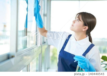 窓を丁寧に拭くエプロン姿の若い女性 窓を丁寧に拭くエプロン姿の若い女性 140440543