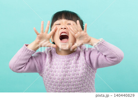 A playful young girl shouting with her hands framing her mouth against a green background. 140440829