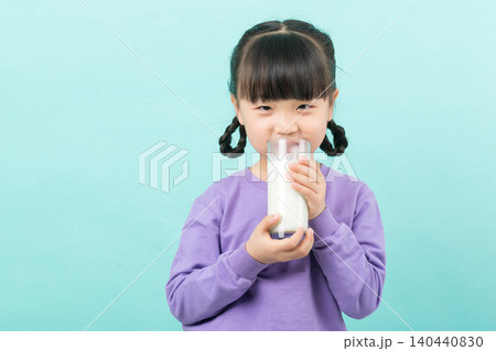 Little Asian girl drinking a glass of fresh milk for calcium and healthy growth, mint green background. 140440830