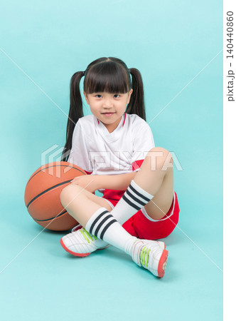 Studio backdrop: A little Asian girl sits on the floor holding a basketball, emphasizing children's sports and outdoor activities. Studio backdrop: A little Asian girl sits on the floor holding a basketball, emphasizing children's sports and outdoor activities. 140440860