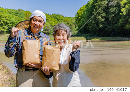 収穫した農産物を手に笑顔でガッツポーズするシニア夫婦 140441017