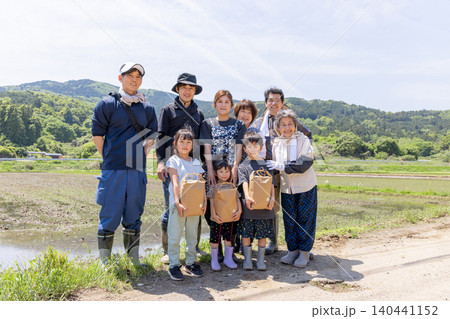 田植え後の水田で収穫物を手に笑顔を見せる三世代家族 田植え後の水田で収穫物を手に笑顔を見せる三世代家族 140441152