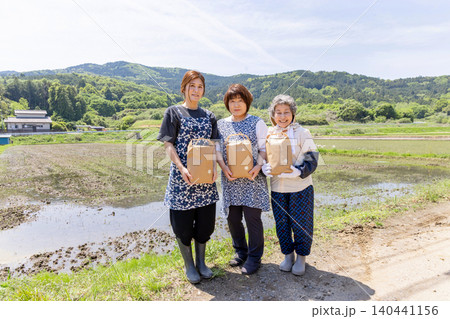 収穫した農産物を手に田んぼで微笑む三世代の日本人女性 140441156
