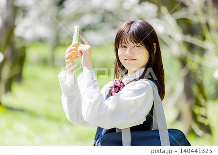 桜の下でスマートフォンを使う女子高校生の春の通学風景 桜の下でスマートフォンを使う女子高校生の春の通学風景 140441325