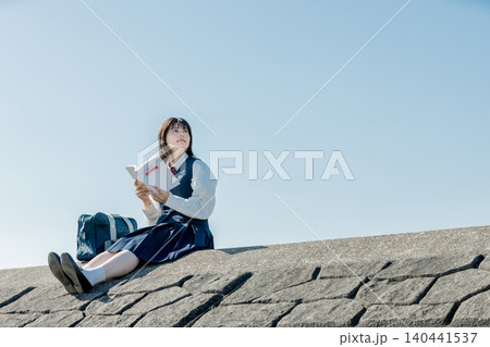 参考書を手に青空の下で学ぶ女子高校生 参考書を手に青空の下で学ぶ女子高校生 140441537