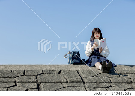 参考書を手に青空の下で学ぶ女子高校生 参考書を手に青空の下で学ぶ女子高校生 140441538