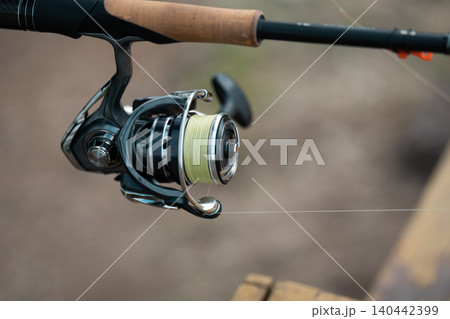 Close view of a fishing reel with fishing line visible by a river 140442399