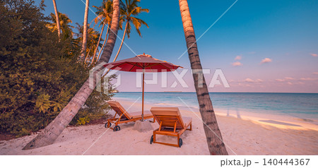 Stunning tropical sunset beach with palm trees, umbrella and loungers. Golden twilight over a calm tropical shore. Romantic paradise resort scene at evening glow. Inspirational summer vacation travel  140444367
