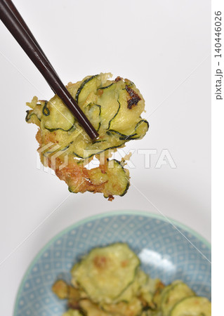 Fried zucchini fritter held with chopsticks over a blue patterned plate Fried zucchini fritter held with chopsticks over a blue patterned plate 140446026