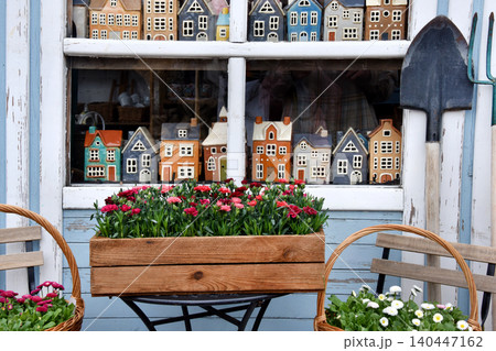 Shop window display of miniature houses and spring flowers with garden tools outside cottage store Shop window display of miniature houses and spring flowers with garden tools outside cottage store 140447162