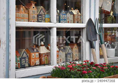 Shop window display of miniature houses and spring flowers with garden tools outside cottage store Shop window display of miniature houses and spring flowers with garden tools outside cottage store 140447168
