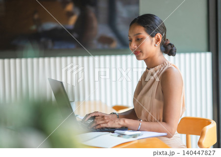 Businesswoman typing on a laptop at an office desk with financial paperwork, highlighting digital work, accounting tasks, business planning, productivity, remote work, and data review. Businesswoman typing on a laptop at an office desk with financial paperwork, highlighting digital work, accounting tasks, business planning, productivity, remote work, and data review. 140447827