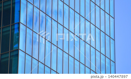 Modern office building with glass facade on a clear sky background. Transparent glass wall of office building. Modern office building with glass facade on a clear sky background. Transparent glass wall of office building. 140447897